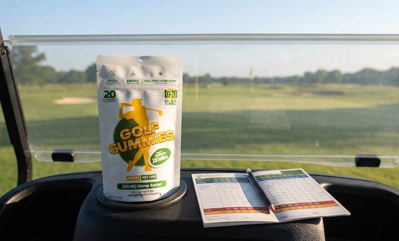 Golf Gummies pouch on a golf cart dashboard next to a scorecard and pencil, sunny fairway ahead — fueling focus for a round of golf